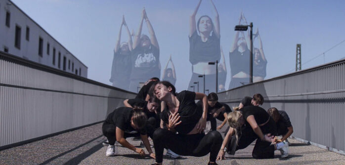 Jugendliche in schwarzer Kleidung bei einer Tanzperforemance auf einer Fußgängerbrücke.