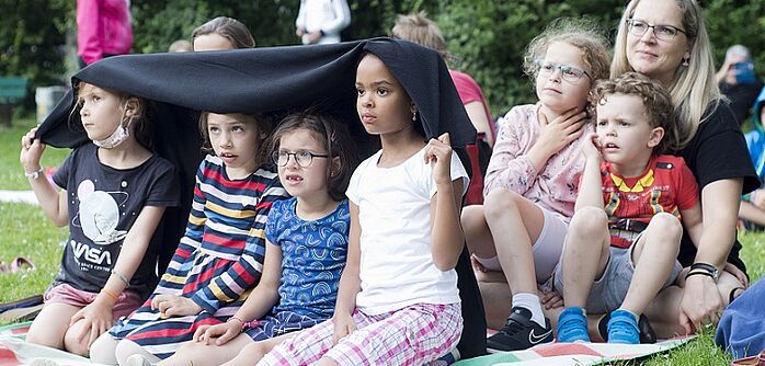 Kulturraum München Kindertheater 2 Kindergruppe unter einer Decke auf der Wiese schauen Theater