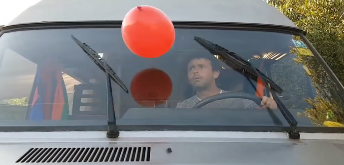 Ein Mann schaut durch die Windschutzscheibe seines Fahrzeugs auf einen roten Lufballon.