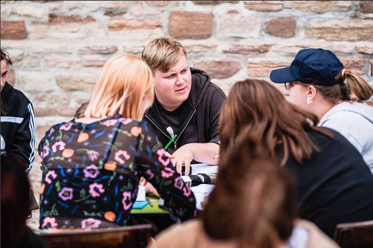 Mehrere junge Erwachsene, die zusammen an einem Tisch sitzen und sich unterhalten