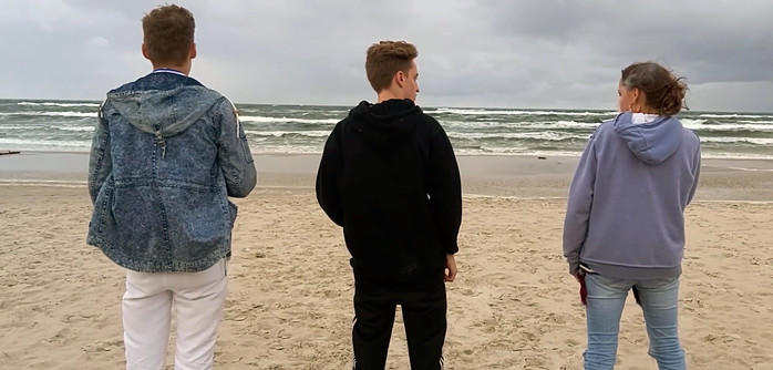 Drei junge Menschen stehen am Strand und schauen aufs Meer.